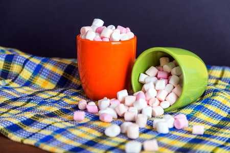 Pink and white marshmallows spilling from a green cup, over blue and yellow waffle towel background. Shallow depth of fieldの写真素材