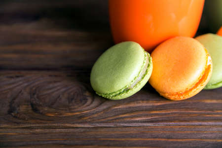 Close view at orange and green french pistachios and orange macaroons in dark colors on a wooden background. Shallow depth of field. Focus at first macaroon.の写真素材