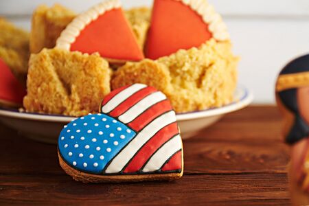 Close view at figures of gingerbread american flag in a heart shape with Thanksgiving pumpkin pie on a wooden background and part of cookie in blur. Shallow depth of fieldの写真素材