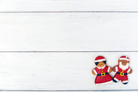 Christmas background with male and female gingerbread men dressed like santa holding hands at the right corner on a white wooden background. A lot of copy space. Top view.の写真素材