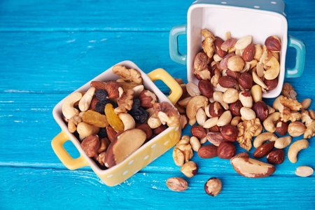 Top view at a scattered mixture of various nuts in a dotted ceramic bowl in a blue wooden background