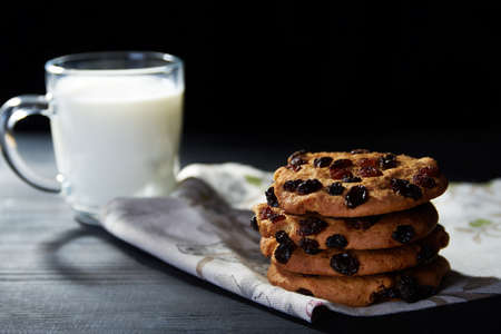 Close view at cookies with raisins and a glass of milk on a dark background with dark dramatic lightの写真素材