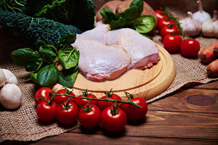 Top view at variety of fresh vegetables, raw chicken legs, eggs and nuts on a burlap cloth and a wooden background with copy space. Selective focus. One source of lightの写真素材