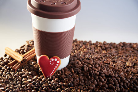 Takeaway brown ceramic cup with cinnamon and gingerbread heart shaped cookies. Scattered coffee...