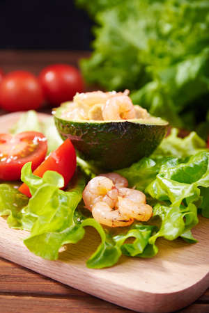 avocado salad with shrimps, tomato and salad on a wooden background with vegetables on a back. Vertical shotの写真素材