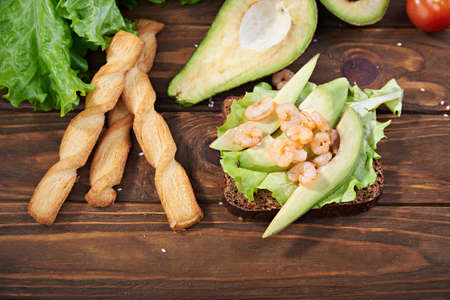 Rye bread sandwich with shrimp, avocado, tomatoes and breadsticks on a wooden backgrpundの写真素材
