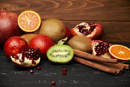 assorted tangerine kiwi apple orange and pomegranate on rustic wooden table with cinnamon sticks....