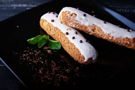Two exquisite cream dessert eclair with fresh mint leaves on a black plate. Shallow depth of fieldの写真素材