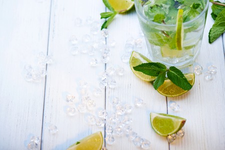 Scattered ice, lime and mint with cold fresh lemonade drink with slice of lime on the glass. Slices of lime and mint leaves on a  white wooden backgroundの写真素材