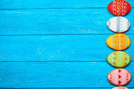 Colorful easter cookies in pink spade in egg shape on blue wooden background at right. With a lot of...