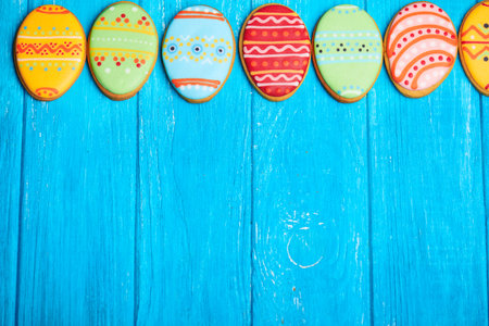 Colorful easter cookies in pink spade in egg shape on blue wooden background at the top. With a lot...