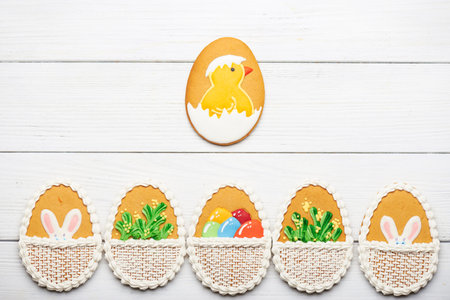 Colorful easter cookies with different pattern in egg shape on white wooden background at the bottom. Big cookie egg with a chicken in the center. Top viewの写真素材