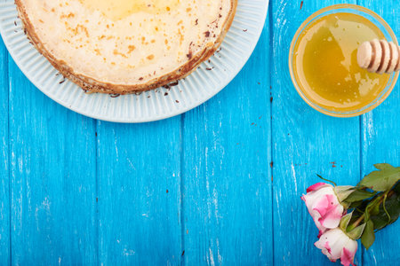 Top view at stack of golden delicious pancakes, honey, rose, cream, romantic breakfast. On a blue...