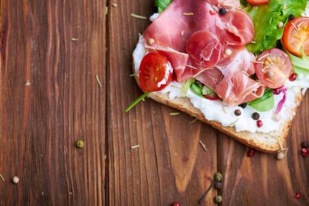Half of sandwiches with prosciutto, tomato, salad and soft cheese on a wooden rustic background. With copy space.の写真素材