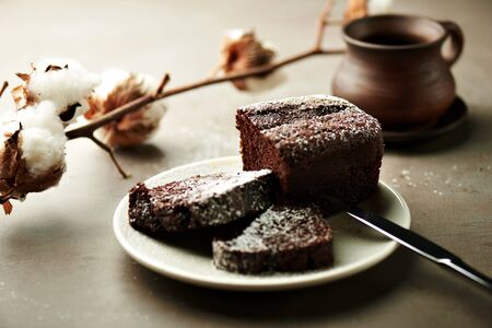Tasty chocolate cake on a white plate, with ceramic cup and cotton flowers on a grey backgroundの写真素材