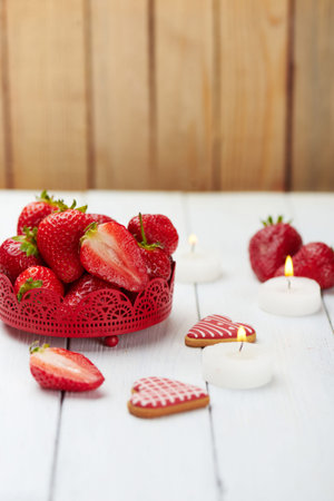 Juicy fresh strawberry with heart shaped cookies, candle and ice on a white wooden background. Romantic set. Strawberry in a bowl. Copy space. Vertical shotの写真素材