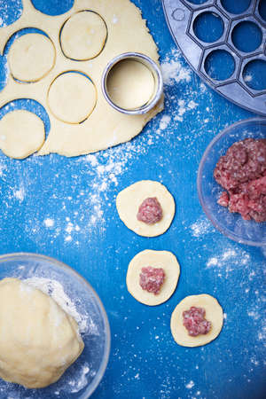 Pelmeni - Russian ravioli. Cooking process with forcemeat on a blue wooden background. Flour is scattered on table. Selective focus.の写真素材