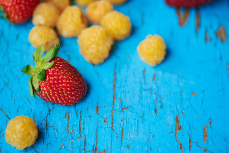 Organic yellow ripe raspberries, pineapple variety, and organic strawberries scattered on a old...