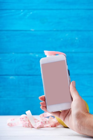 Women takes photo with smarphone with empty screen. Water and measurement tape - diet and sport eating concept. On a wooden background. Shooting for social mediaの写真素材