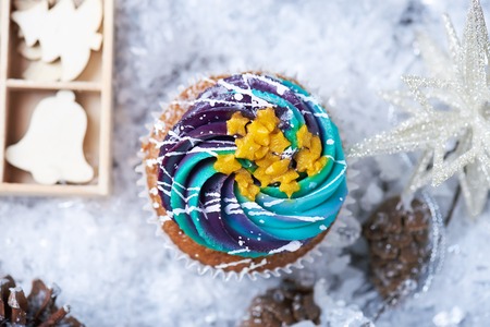 Winter cupcakes with gradient cream and golden stars on a snow with presents, wooden toys, cone and snowflakes on a background. Winter mood. Top viewの写真素材