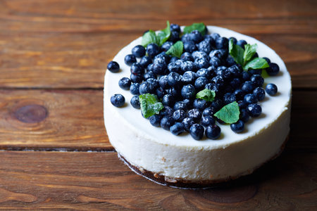 Sweet creamy blueberry cheesecake with fresh blueberries and mint leaves on a wooden background with...