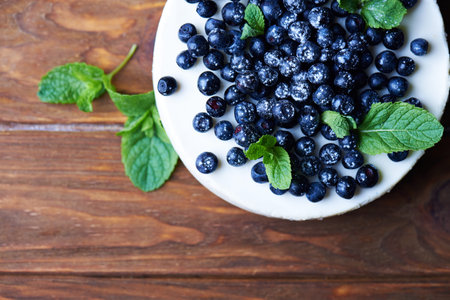Sweet creamy blueberry cheesecake with fresh blueberries and mint leaves on a wooden background with copy space. top view.の写真素材