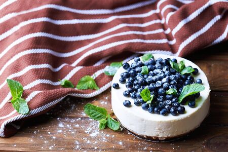 Sweet creamy blueberry cheesecake with fresh blueberries, mint leaves and a towel on a wooden background with copy space.の写真素材