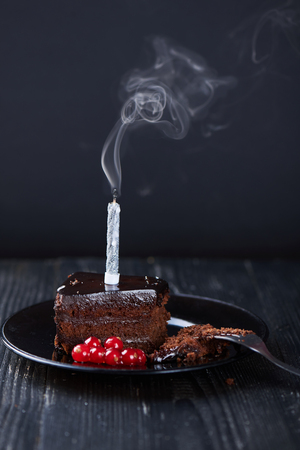 A slice of chocolate cake with redcurrant fork and a single extinguished candle on a dark background. Vertical shotの写真素材