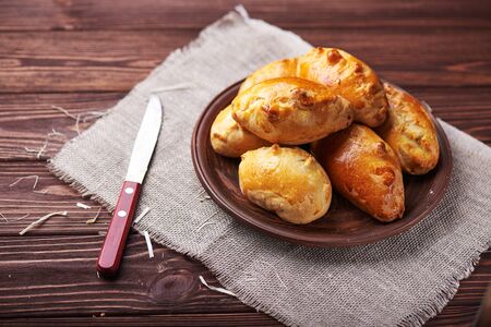 Delicious rustic pastries filled with meat and vegetables on a ceramic plate with wooden knife on a wooden background.の写真素材