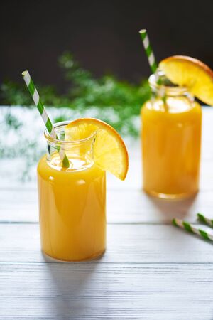 Fresh orange juice in the jar with straw on white wood table. Vertical shotの写真素材