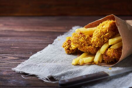 Crispy fried chicken breast with french fries to go on an old rustic wooden background with a sackcloth napkin. Close-up. With copy space.の写真素材