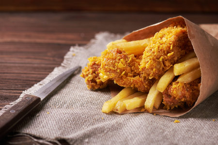 Crispy fried chicken breast with french fries to go on an old rustic wooden background with a...