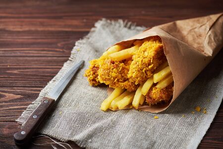 Crispy fried chicken breast with french fries to go on an old rustic wooden background with a sackcloth napkin. Close-up. With copy space.の写真素材