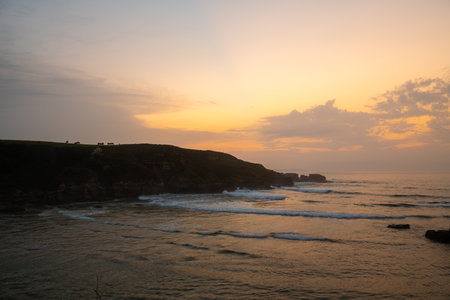 sunset on a beach with silhouettes of cows on the green cliffsの写真素材