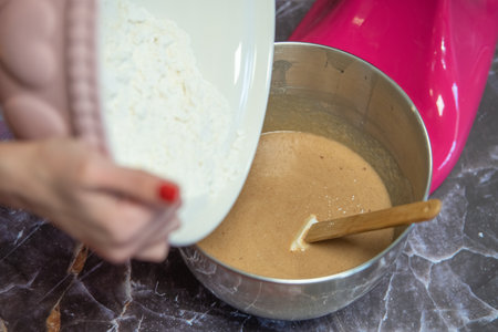 woman's hands pouring flour into a metal bowl for mixerの写真素材