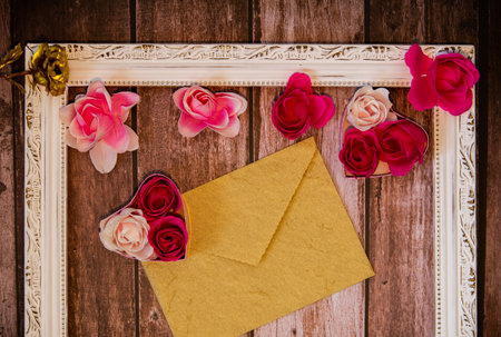 Wooden background with roses, hearts, a closed envelope and a photo frame for Valentine's dayの写真素材