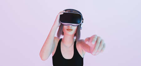 caucasian girl playing with virtual reality goggles pointing with her hand out of focus to the camera with blue and pink lights. 3d renderingの写真素材
