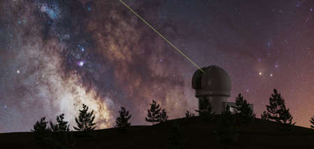 milky way with large telescope on the horizon and pine trees in silhouette and green laser pointing...
