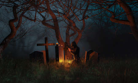 person with cloak praying in a cemetery at night illuminated by candles in a terrifying forest....