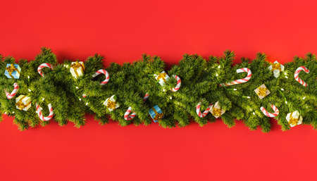 row of Christmas tree garland with gifts and candy ornaments on a deep red background. 3d renderingの写真素材