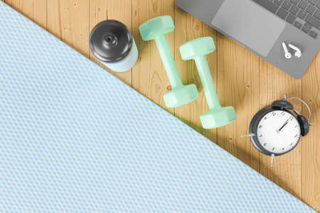 top view of gym mat with laptop, exercise equipment and alarm clock next to it. online training...