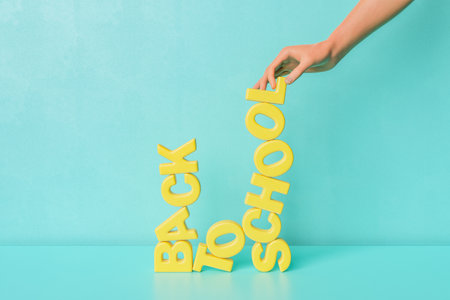 3D rendering of crop unrecognizable person creating Back To School text with yellow letters against blue backgroundの写真素材