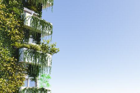 3D illustration of modern block of flats covered with lush green plants against cloudless blue sky in cityの写真素材