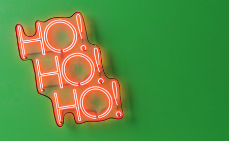 3D illustration of red neon Ho ho ho inscription with exclamation marks hanging on green wall during Christmas celebrationの写真素材