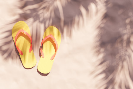 3D rendered image of from above bright yellow slippers placed on sandy ground against shade of palm leavesの写真素材