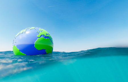 plastic sphere of planet earth floating in the ocean with underwater view and clear sky. copy space....