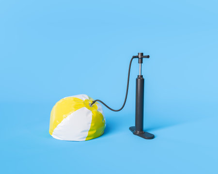3d rendering of a deflated yellow and white beach ball attached to a black pump on a blue...