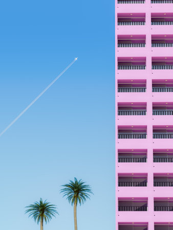 3d rendering of a minimalist scene with a clear blue sky, an airplane in flight, two palm trees, and the side of a pink apartment building. Vacation concept.の写真素材