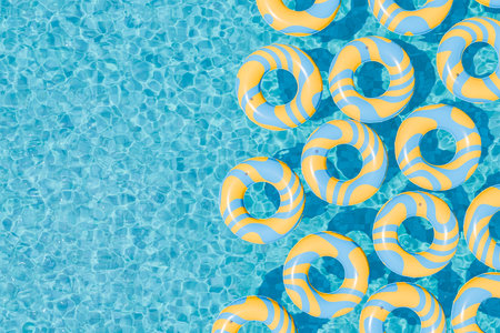 3D rendering of multiple yellow and blue striped inflatable rings floating on the clear blue water of a swimming pool. Leisure and summer concept.の写真素材