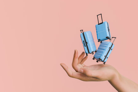 Hand balancing multiple falling miniature blue suitcases with wheels against a red background. Travel and vacation concept. 3d rendering.の写真素材